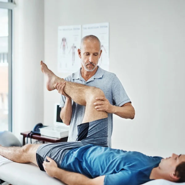 Un homme se fait examiner la jambe par un physiothérapeute dans un cadre professionnel de réhabilitation.