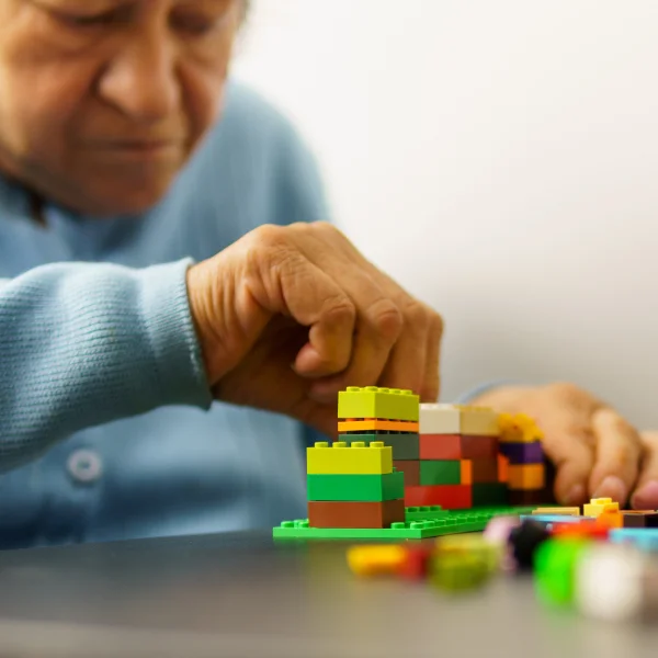 Une femme âgée s'amuse à assembler des Lego, illustrant l'ergothérapie en santé mentale.