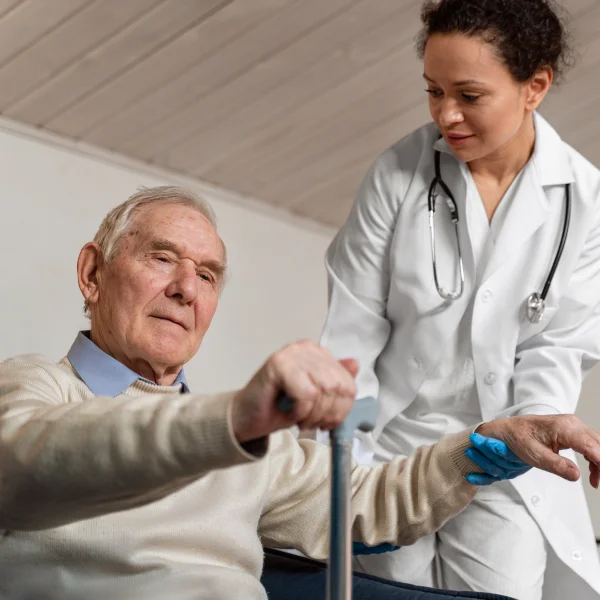 A doctor assists an elderly man using a cane, providing support and guidance in a medical setting.